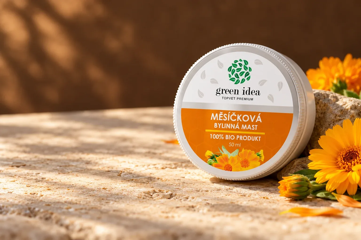 Pôvodný téglik nechtíkovej masti Green idea s oranžovou etiketou a kvetmi nechtíka na svetlom kameni