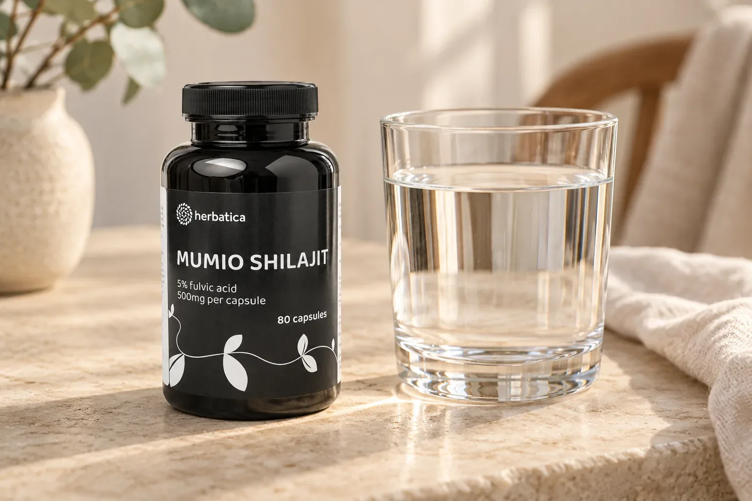 Shilajit Herbatica v pôvodnom čiernom balení vedľa pohára vody